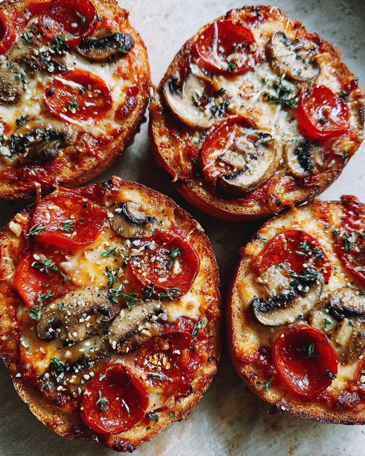 Four perfectly toasted English muffin pizza halves topped with melted cheese, pepperoni, mushrooms, and herbs.