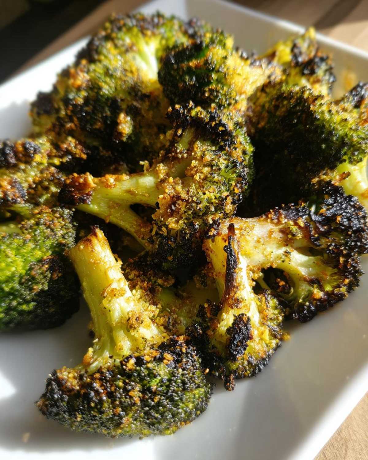 Close-up of perfectly seasoned and crispy roasted broccoli florets on a white plate.