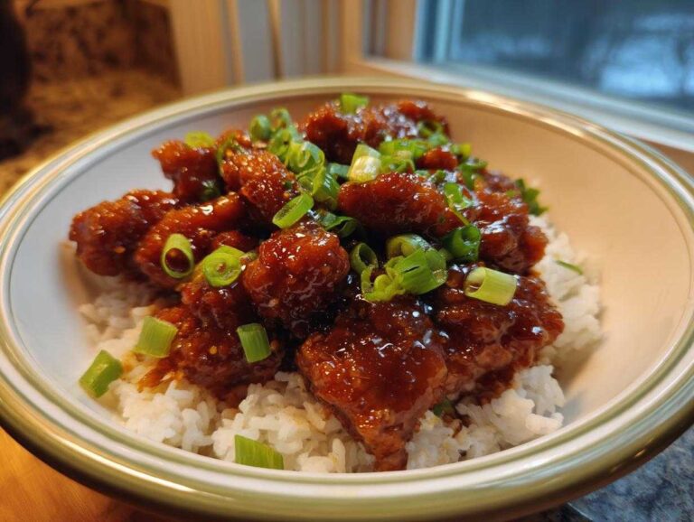 Amazing Crockpot Bourbon Chicken Flavor Now A bowl filled with white rice topped with saucy Crockpot Bourbon Chicken and garnished with sliced green onions.