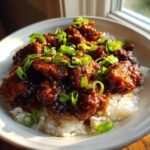 Close-up of saucy Crockpot Bourbon Chicken pieces served over fluffy white rice and garnished with fresh green onions.