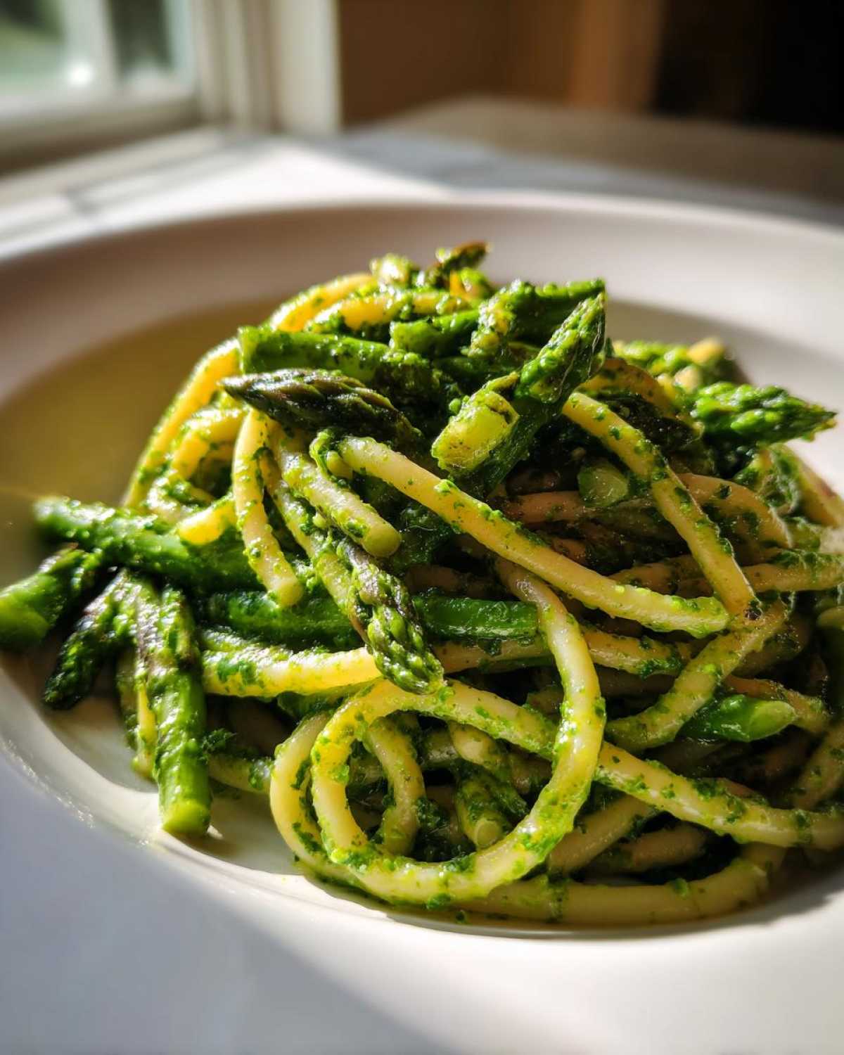 Close-up of bright green Earth Day Dinner Pasta tossed with asparagus tips and pesto sauce in a white bowl.