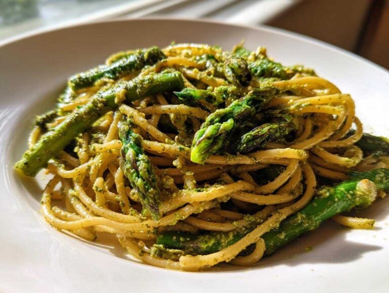 A close-up of Earth Day Dinner Pasta featuring spaghetti tossed in green pesto sauce with bright green asparagus spears.