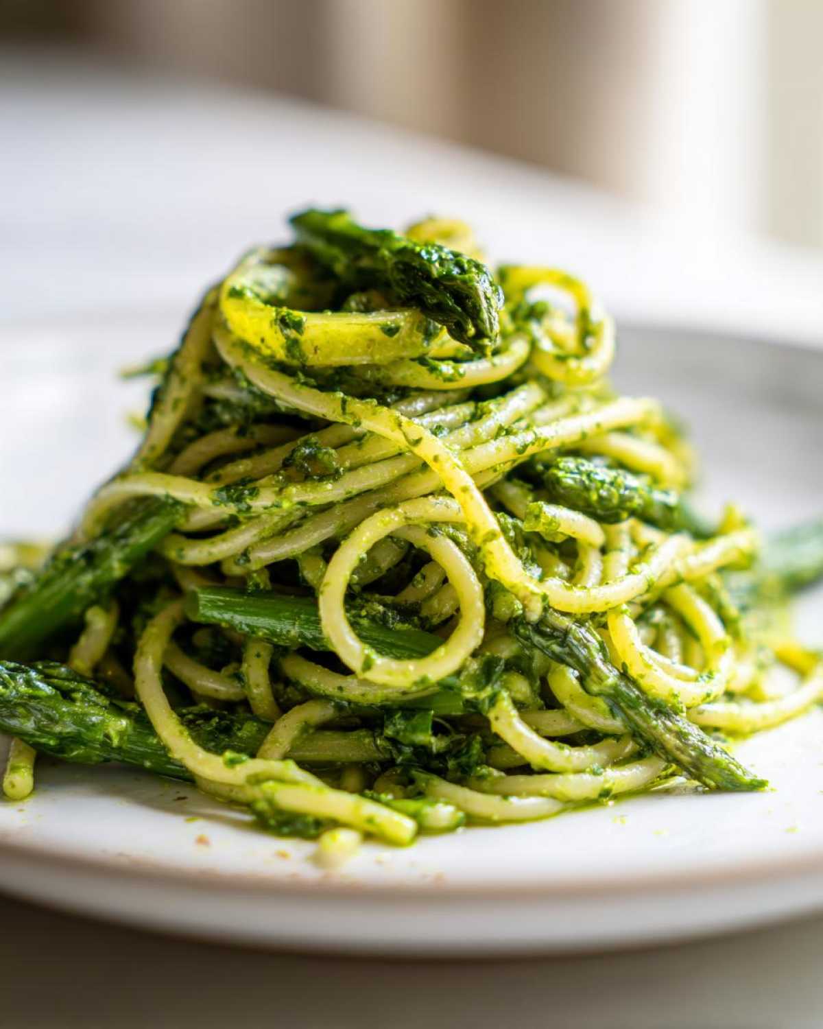 Close-up of a serving of Earth Day Dinner Pasta, featuring spaghetti tossed in bright green pesto with chunks of fresh asparagus.