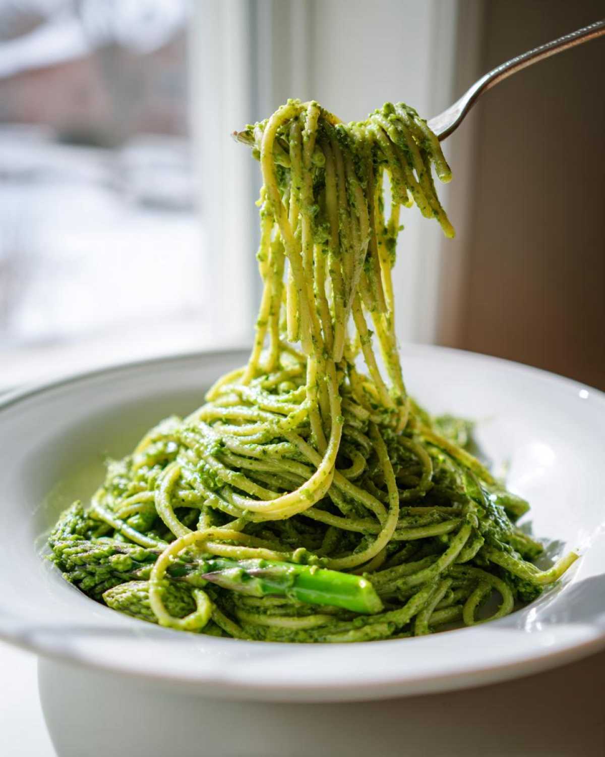 A fork lifting spaghetti coated in vibrant green pesto, served in a white bowl, showcasing the Earth Day Dinner Pasta.