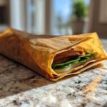 A sandwich wrapped in brown, reusable material, showcasing one of the Eco Friendly Picnic Sandwich Wraps.