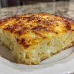 A close-up of a golden-brown, cheesy slice of hashbrown casserole on a white plate.
