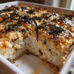 A close-up view of a freshly baked sushi bake casserole, showing the creamy topping, rice base, and nori strips.