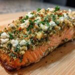 A close-up of a perfectly baked Feta and Herb Crusted Salmon fillet resting on a wooden cutting board.