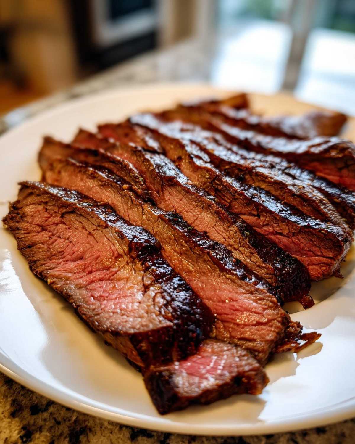 Close-up of medium-rare Flank Steak with Soy Marinade, sliced thinly across the grain on a white plate.