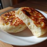 Two halves of a fluffy homemade english muffin showing the signature nooks and crannies, resting on a white plate.