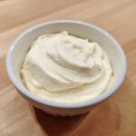 Close-up of a small white bowl filled with fluffy, creamy white fruit dip, resting on a wooden surface.