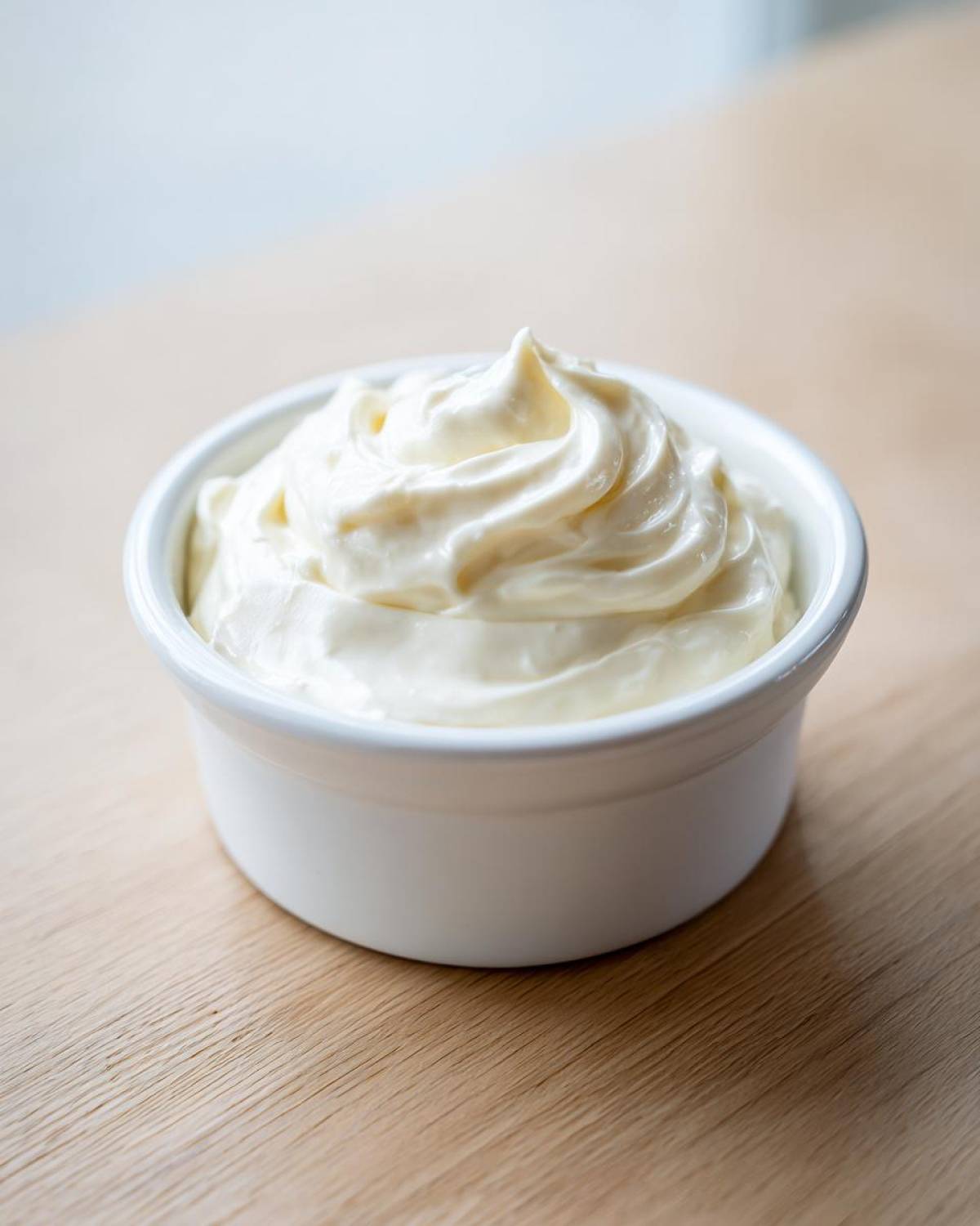 Close-up of fluffy, creamy white fruit dip swirled high in a small white ramekin on a light wooden surface.