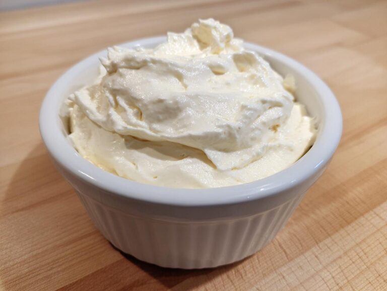 Close-up of fluffy, creamy white fruit dip served in a small white fluted ramekin on a wooden surface.
