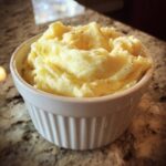 A close-up of creamy, fluffy mashed potatoes seasoned with pepper, served in a white, ribbed ramekin.