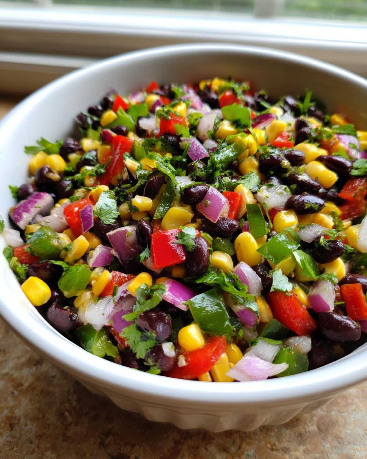 Close-up of vibrant Cowboy Caviar featuring black beans, corn, red onion, bell peppers, and cilantro in a white bowl.