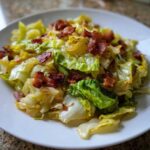 Close-up of perfectly cooked Fried Cabbage with Bacon Onion served on a white plate.