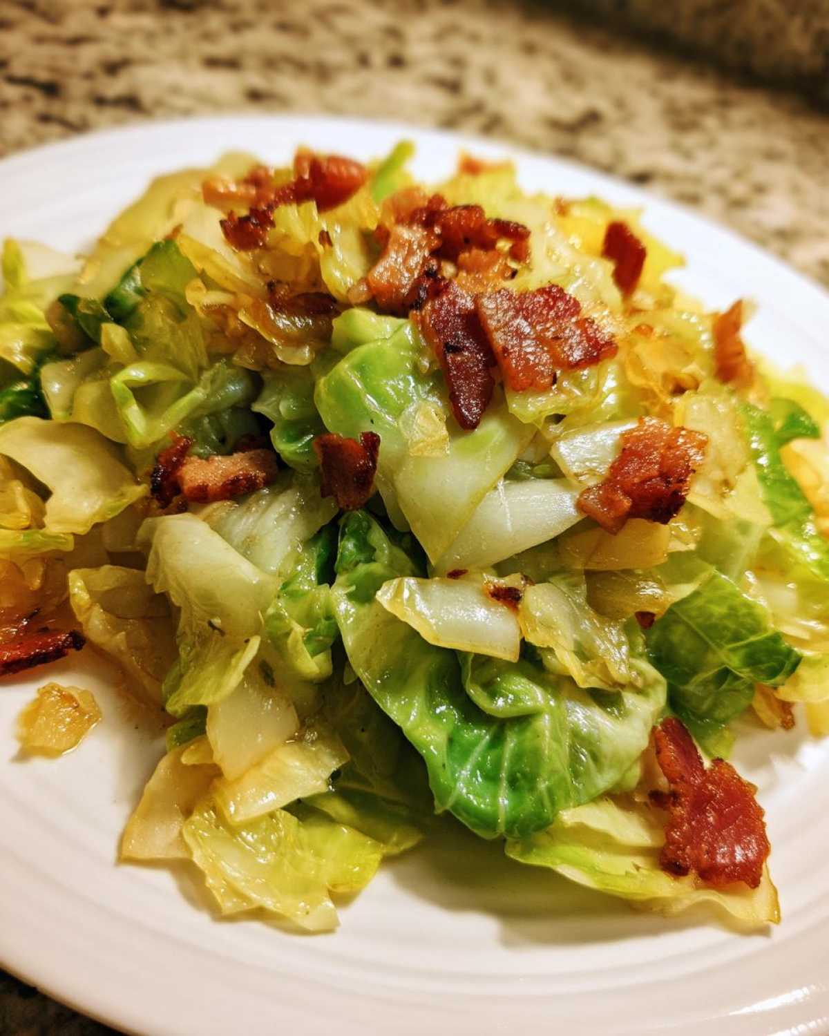 A close-up of delicious Fried Cabbage with Bacon Onion served on a white plate.