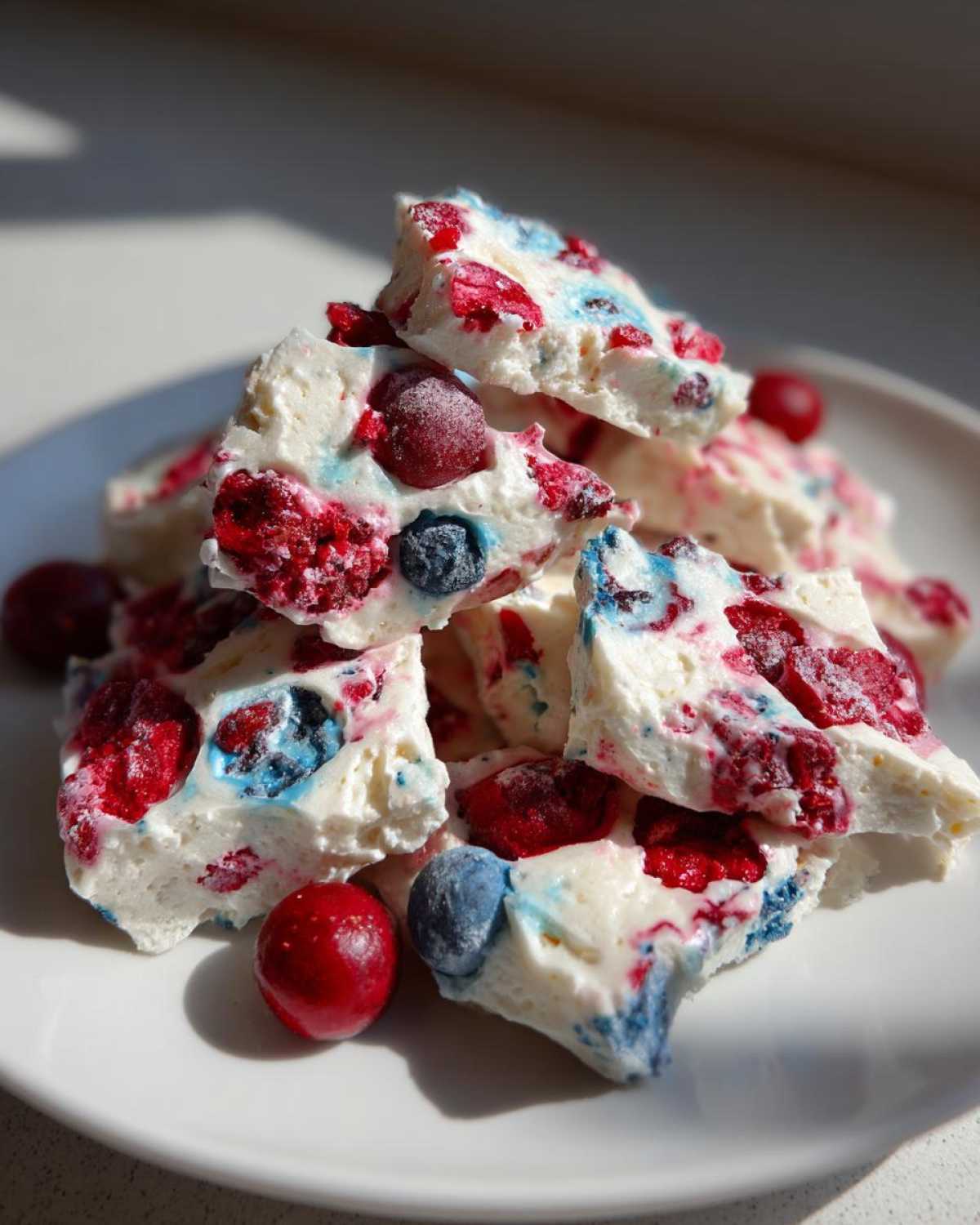 Close-up of broken pieces of Frozen Yogurt Bark with Spring Berries piled on a white plate.