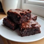 Close-up of four fudgy Banana Bread Brownies stacked on a white plate, showing their rich, dark chocolate texture.