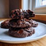 A stack of three fudgy Chocolate Chocolate Chip Cookies, with the top one broken in half to show the gooey interior.