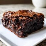 Close-up of a moist, fudgy slice of chocolate cobbler with a crackly top and visible chocolate chips.