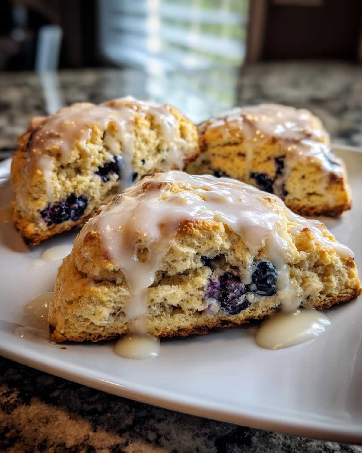 Three freshly baked Blueberry Lemon Scones Recipe pieces drizzled with thick white lemon glaze.
