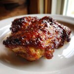 Two pieces of perfectly glazed Honey Garlic Chicken Thighs with a shiny, sticky, caramelized coating on a white plate.