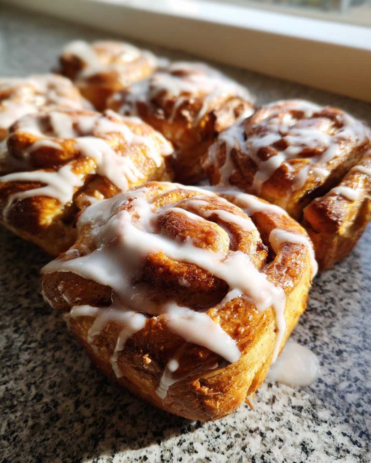 A close-up of several freshly baked Sourdough Cardamom Buns drizzled with white icing.