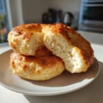 Three golden-brown Cottage Cheese Bagels stacked on a plate, one broken in half showing the soft interior texture.