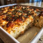 Close-up of a freshly baked sushi bake casserole with a golden-brown top and shredded nori, showing a scoop removed.