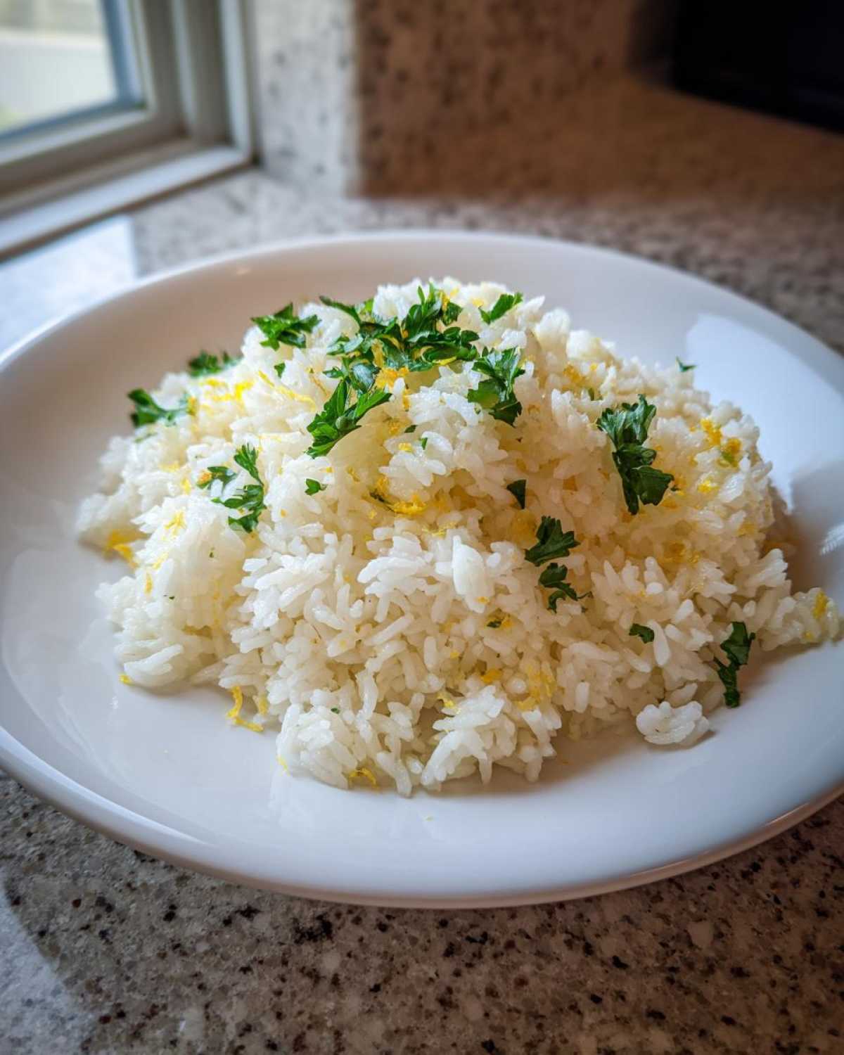 A white bowl filled with fluffy Greek Lemon Rice, topped with fresh parsley and bright yellow lemon zest.