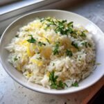 A white bowl filled with fluffy Greek Lemon Rice, topped with bright yellow lemon zest and fresh chopped parsley.