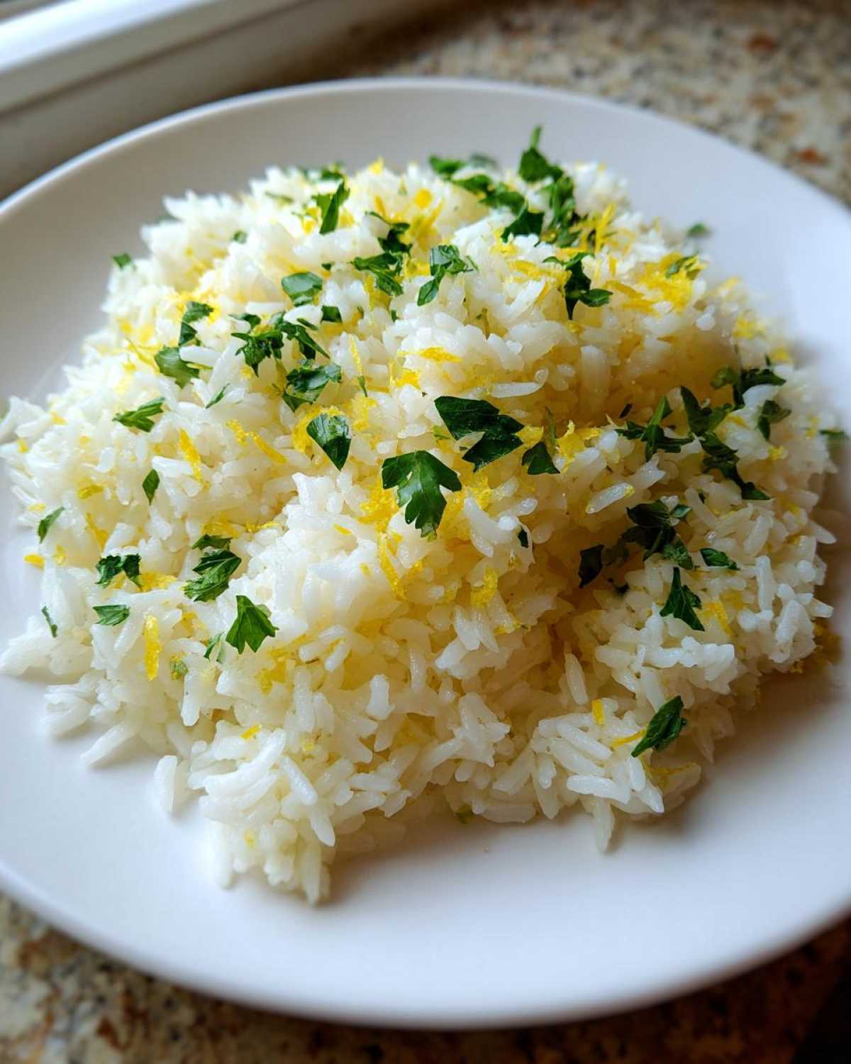 A close-up of fluffy Greek Lemon Rice topped with bright yellow lemon zest and chopped fresh parsley.
