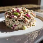 A molded serving of healthy tuna salad featuring visible chunks of red onion and celery on a white plate.