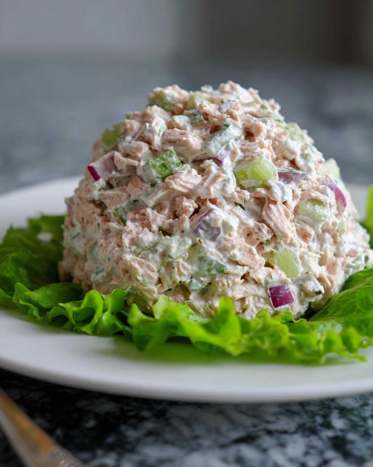 A scoop of creamy healthy tuna salad mixed with celery and red onion, served on a bed of crisp green lettuce.