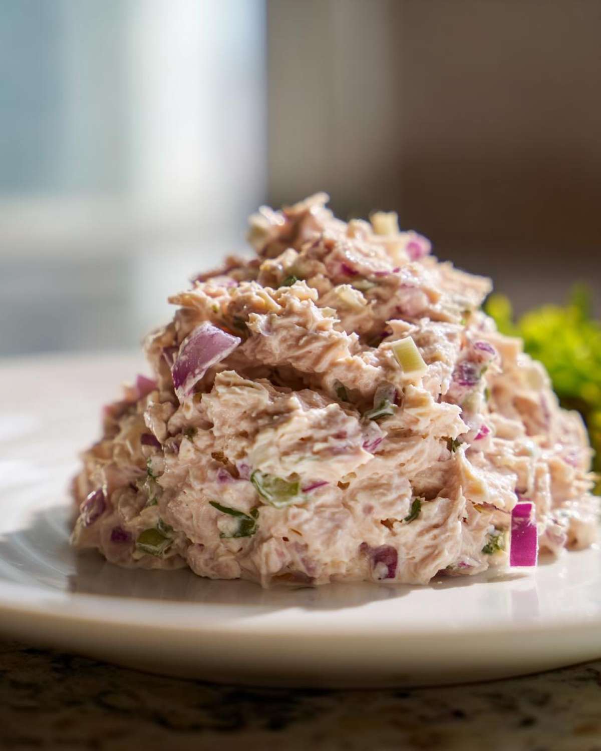 Close-up of a generous mound of healthy tuna salad mixed with visible chunks of red onion and celery on a white plate.