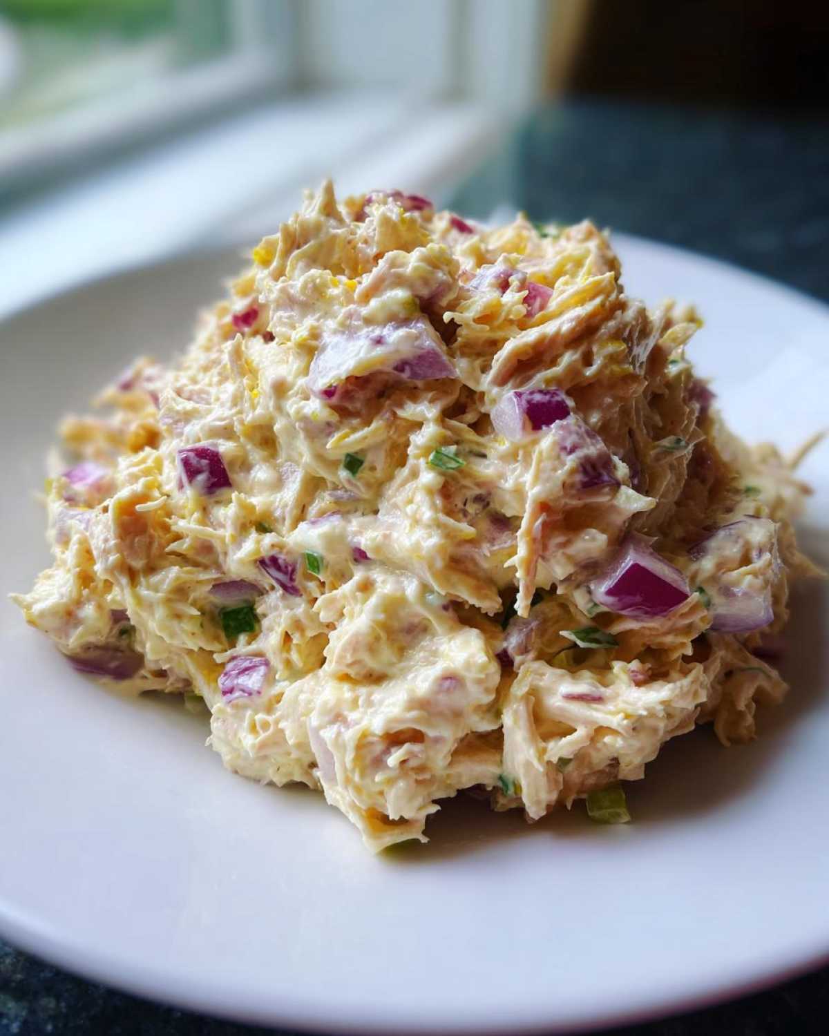 A mound of creamy healthy tuna salad mixed with visible chunks of bright red onion served on a white plate.