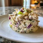 A mound of creamy healthy tuna salad mixed with visible chunks of red onion and celery served on a white plate.