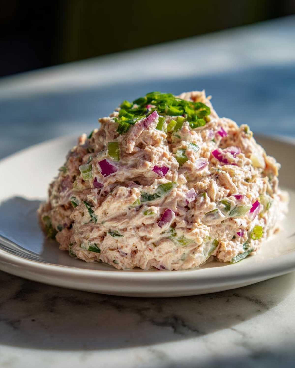 A generous scoop of healthy tuna salad mixed with visible chunks of red onion and green celery, topped with fresh chives.