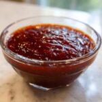 Close-up of thick, rich, homemade bbq sauce glistening in a small clear glass bowl.