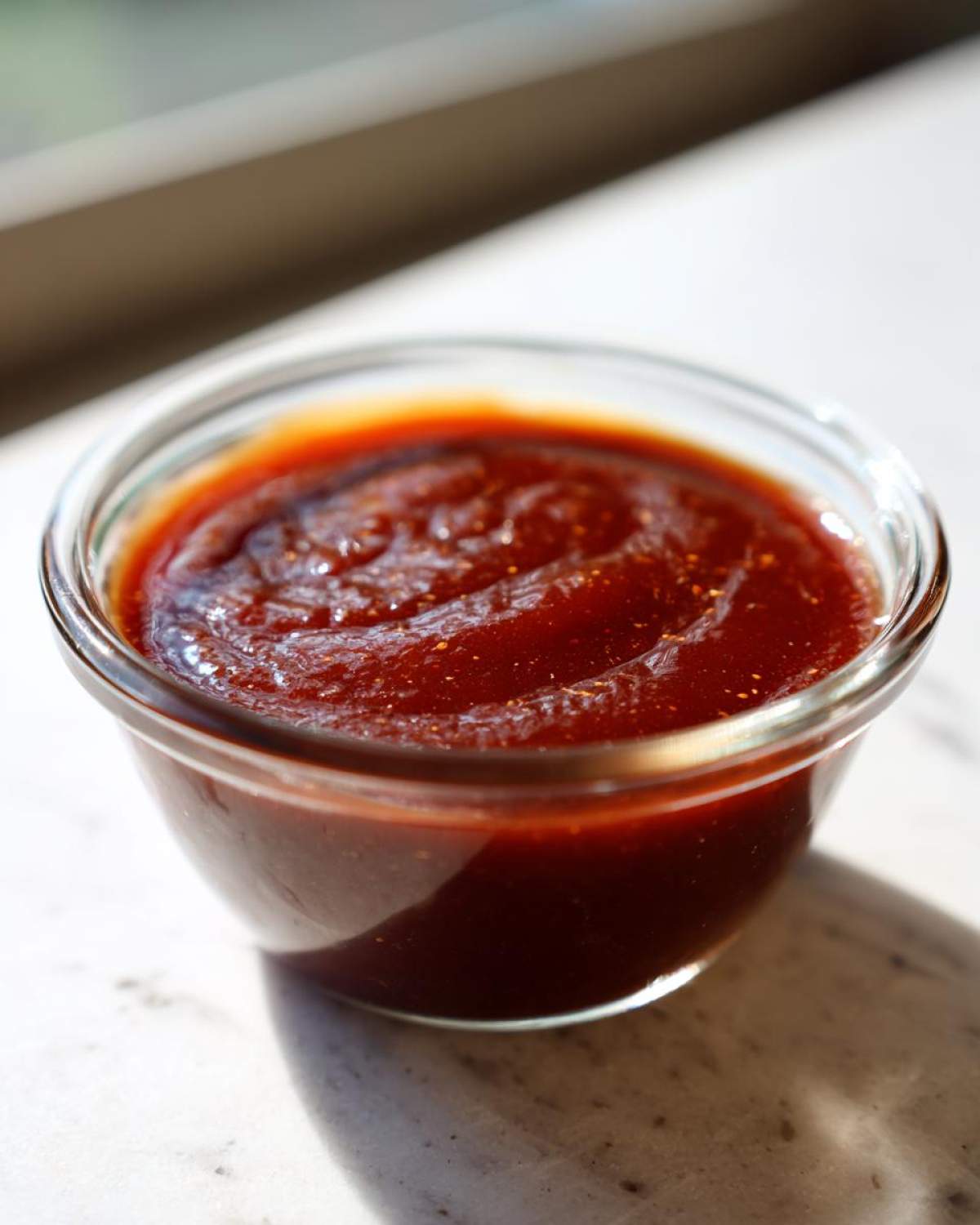 Close-up of thick, dark red homemade bbq sauce in a small clear glass ramekin.