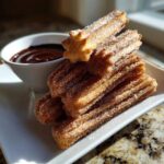 A stack of freshly made Homemade Churros with Chocolate Sauce, coated in cinnamon sugar, served on a white plate.