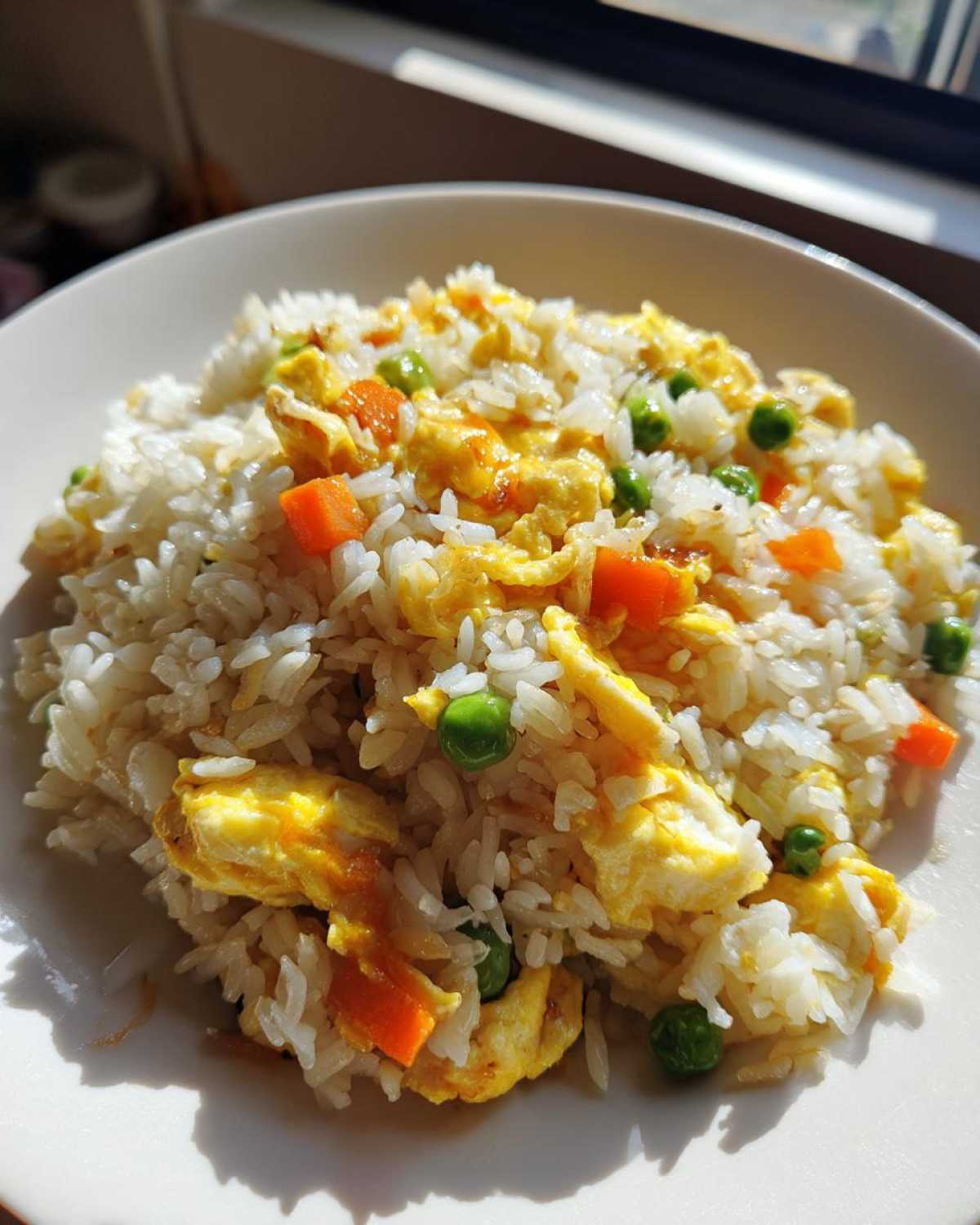 Close-up of a bowl of homemade Egg Fried Rice featuring white rice, scrambled egg pieces, bright green peas, and diced carrots.