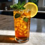 A tall glass filled with Homemade Iced Tea with Fresh Herbs, ice, mint sprigs, and a lemon slice garnish.