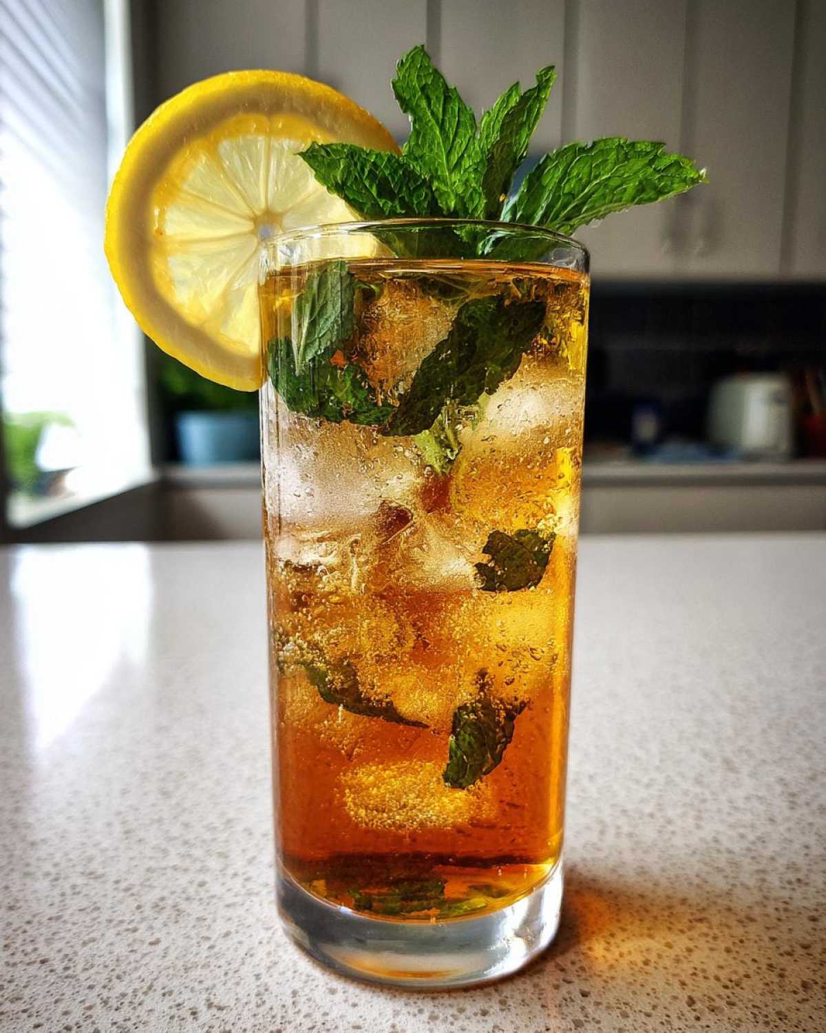 Tall glass of Homemade Iced Tea with Fresh Herbs, ice, mint sprigs, and a lemon slice garnish.