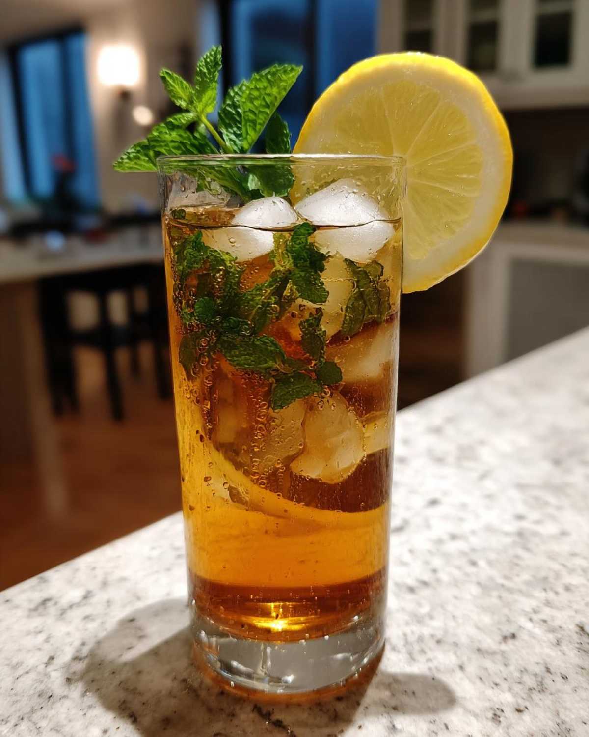 A tall glass of Homemade Iced Tea with Fresh Herbs, filled with ice, mint leaves, and garnished with a lemon slice.
