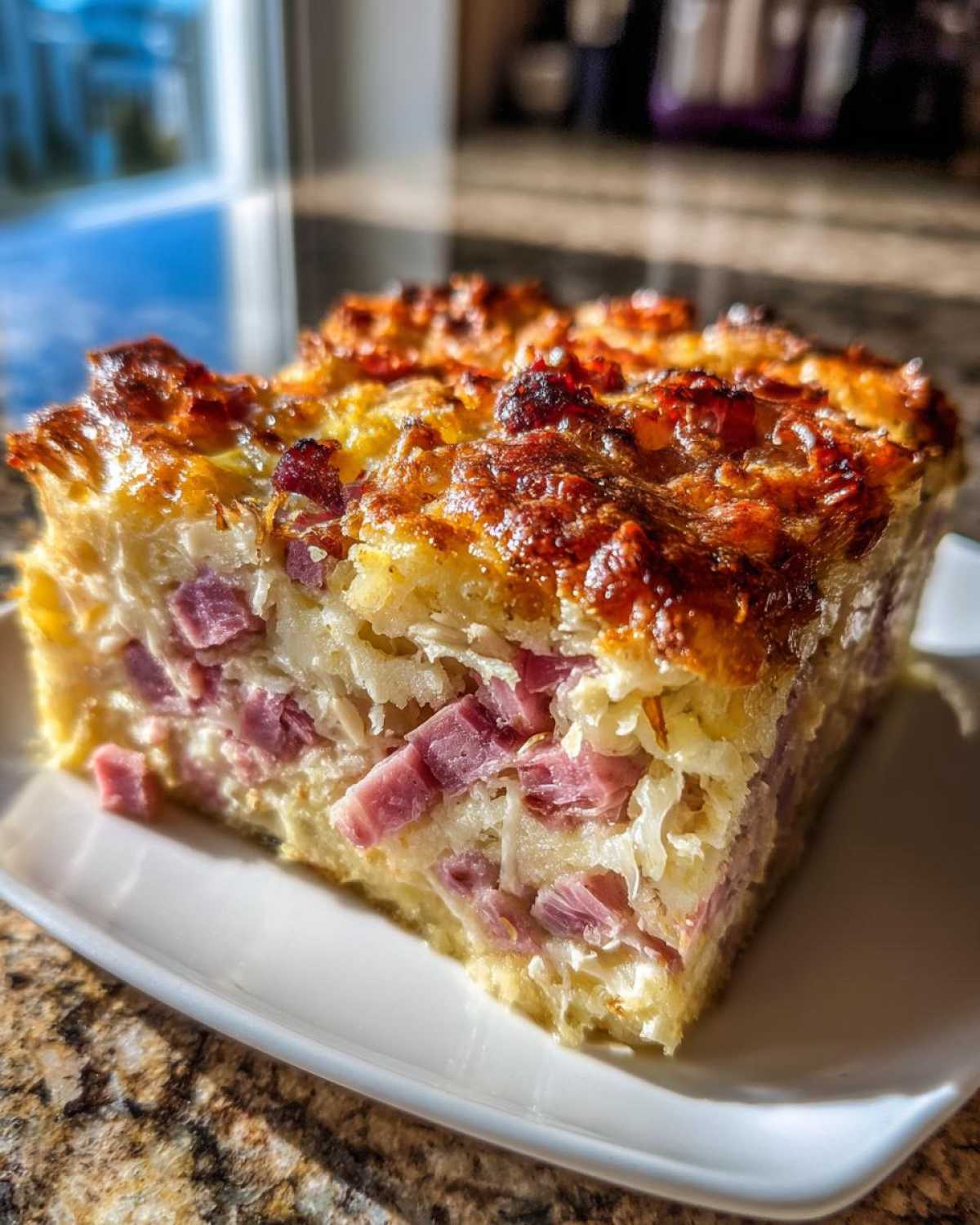 A close-up square slice of homemade Reuben bake showing layers of ham, sauerkraut, and a golden, cheesy top.
