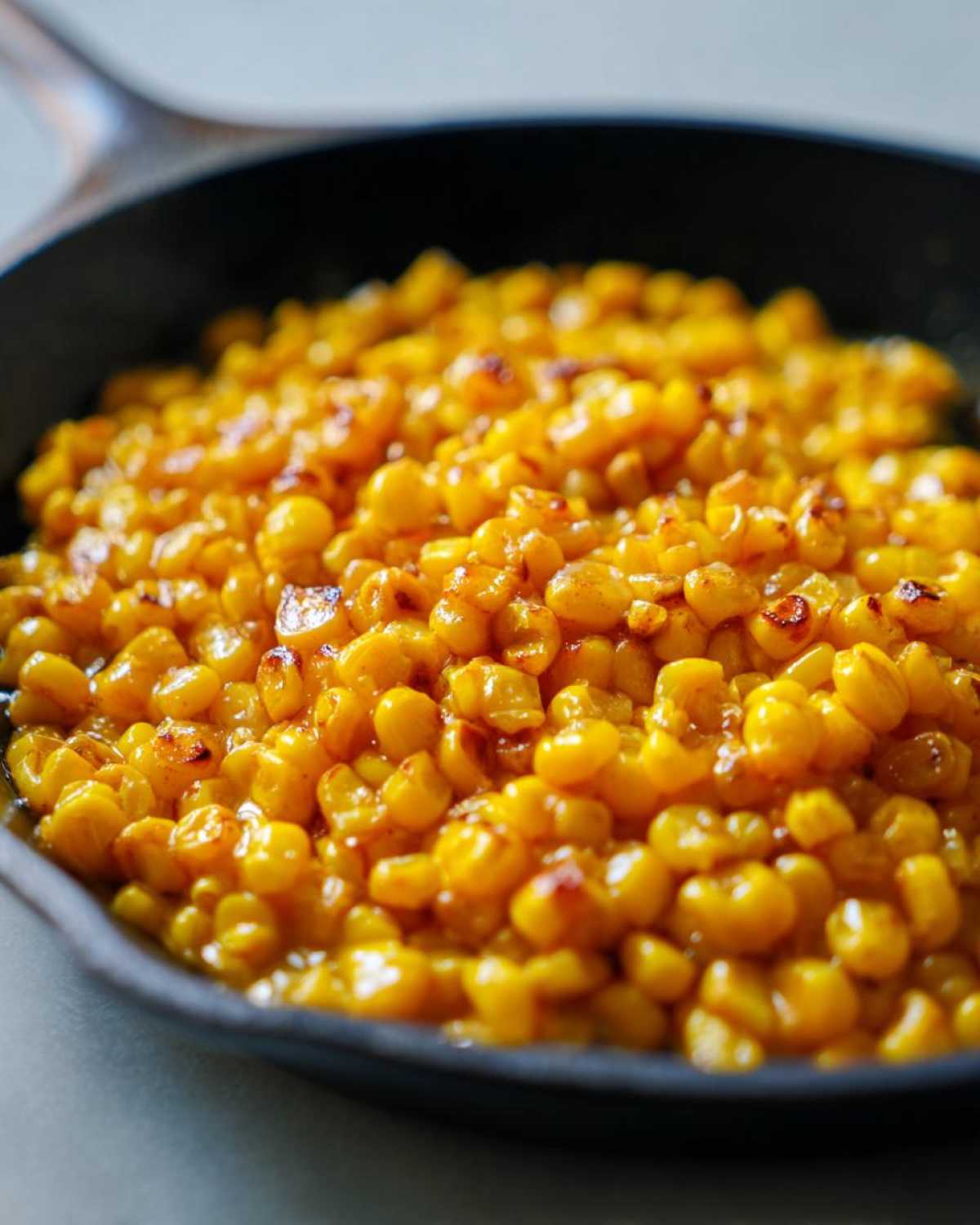 Close-up of sweet, caramelized kernels of Honey Butter Skillet Corn sizzling in a dark cast iron pan.