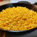 Close-up of bright yellow corn kernels simmering in a rich glaze inside a black cast iron skillet, ready to serve as Honey Butter Skillet Corn.