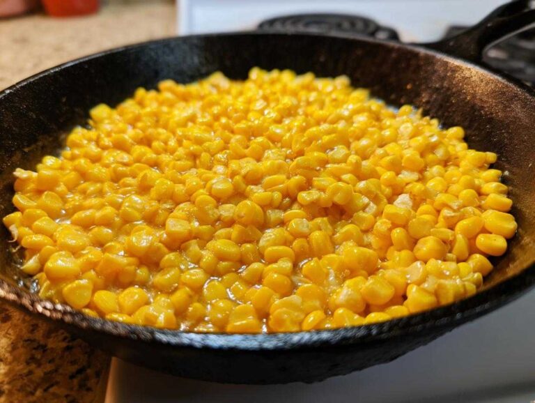 Close-up of bright yellow corn kernels simmering in a rich glaze inside a black cast iron skillet, ready to serve as Honey Butter Skillet Corn.
